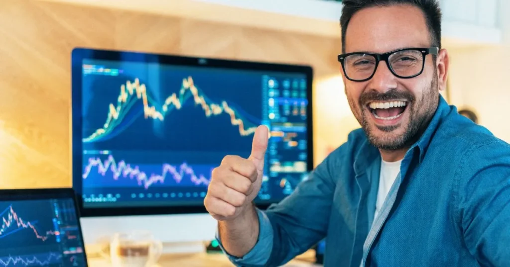 A man smileing and behind him  has two screen, where  showing crypto statistic